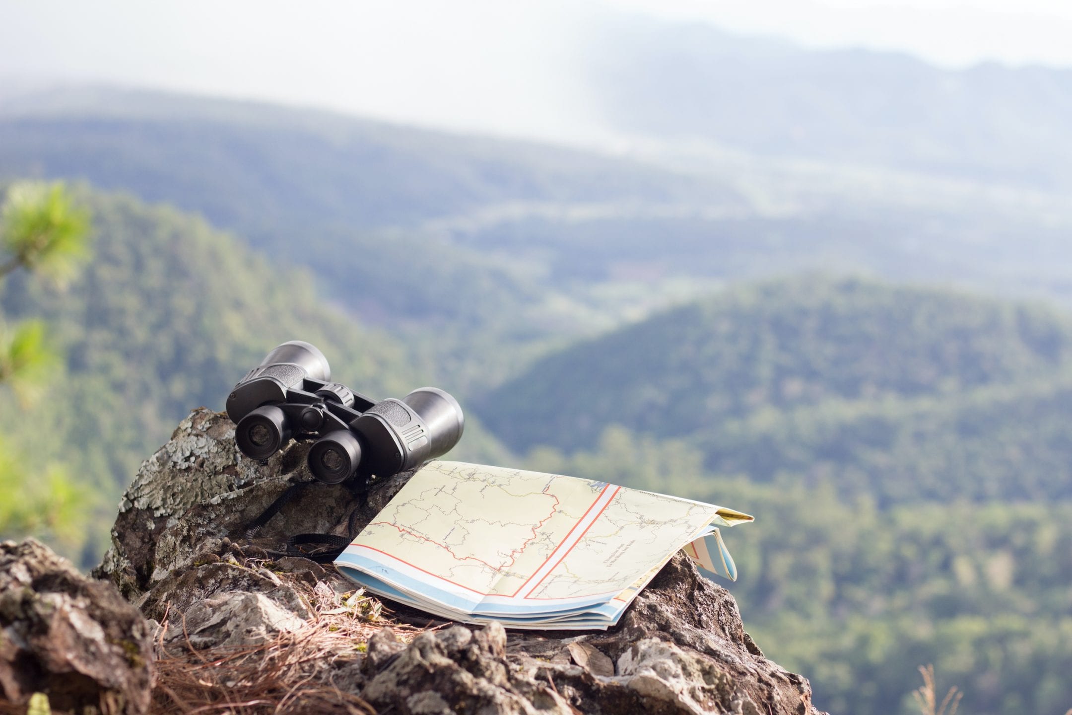 Binoculars and hiking maps on rocky cliffs with landscape